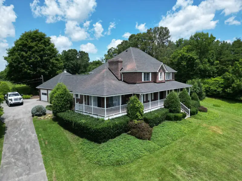 Aerial view of an asphalt shingle roof on a brick home with a wraparound porch — Palisade Roofing, East Tennessee.